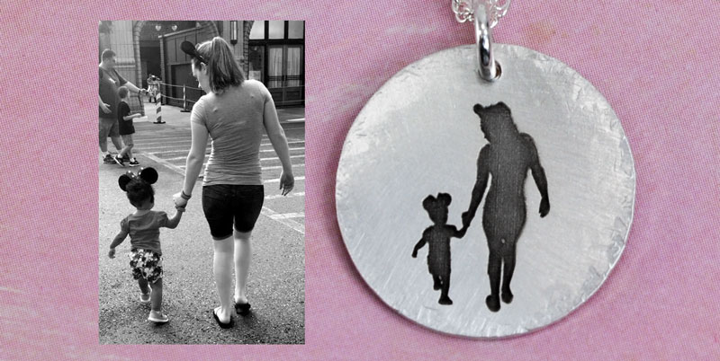 Silhouette on a silver charm showing mom and daughter walking